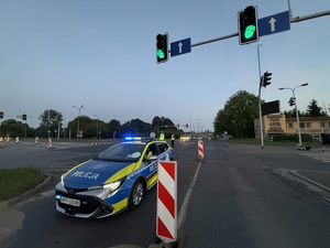 Zdjęcie przedstawia radiowóz policyjny wraz z umundurowanymi policjantami podczas zabezpieczenia I Maratonu Zagłębiowskiego w dniu 23 maja 2026 roku.