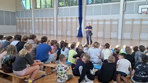 Umundurowany policjant na spotkaniu z dziećmi w szkole podstawowej - sala gimnastyczna wykład.
