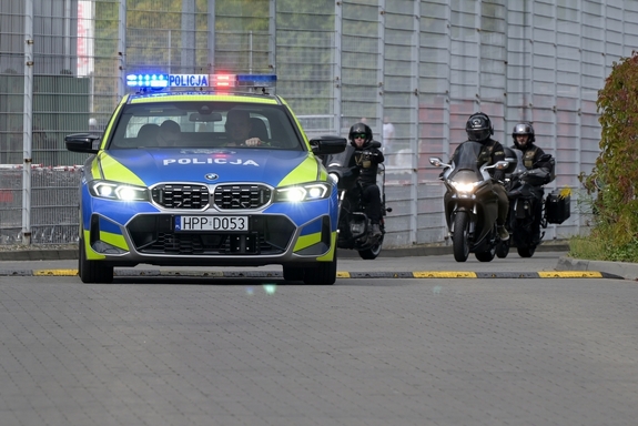 Na zdjęciu widzimy oznakowany radiowóz i motocykle w tle podczas przejazdu ulicami naszego miasta